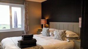 A neatly made bed with patterned pillows and a folded blanket, a bedside lamp, and a window with curtains. - An exceptional place to gather on the sea shore (Newport)