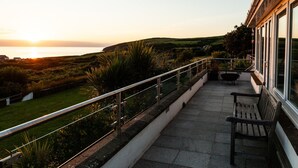 A balcony with a view of the sunset over the sea, a grassy area, and a bench. - An exceptional place to gather on the sea shore (Newport)