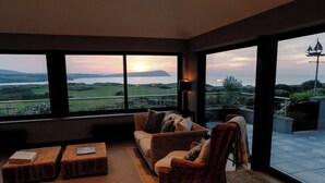 A modern living room with a large window offering a scenic view of a lake and distant hills. - An exceptional place to gather on the sea shore (Newport)
