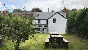 En grönskande trädgård med ett picknickbord och ett vitt hus i bakgrunden.
