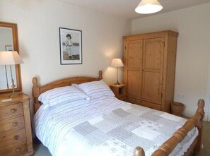 A bedroom with a wooden bed, two bedside tables with lamps, a wooden wardrobe, and a framed picture on the wall.