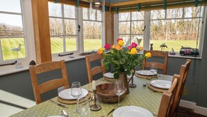 A dining area with a table set for six, featuring a green polka dot tablecloth, wooden chairs, and a vase with flowers. - A beautiful property for 6 with expansive lawns, minutes from the beach (Newport)