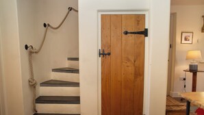 A wooden door with a rope handle, a staircase with white steps, and a small table with a lamp in the background. - A beautiful property for 6 with expansive lawns, minutes from the beach (Newport)