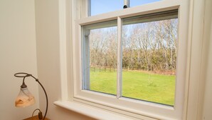 A room with a window overlooking a grassy area and trees. - A beautiful property for 6 with expansive lawns, minutes from the beach (Newport)