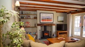 A cozy living room with a fireplace, a television, and a bookshelf. - A beautiful property for 6 with expansive lawns, minutes from the beach (Newport)