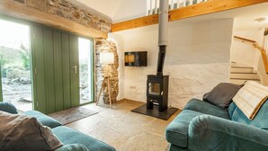 A cozy living room with a stone wall, a green door, a wooden staircase, and a black wood-burning stove.