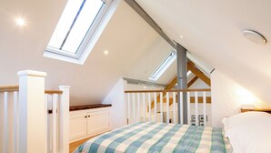 A bedroom with a sloped ceiling, skylights, a bed with a plaid blanket, and white cabinetry.