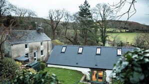 A house with a sloped roof, a small garden, and a view of the surrounding countryside.