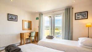 Une chambre d’hôtel avec deux lits, un bureau, une chaise, un panneau indiquant la sortie de secours et une vue sur l’extérieur.