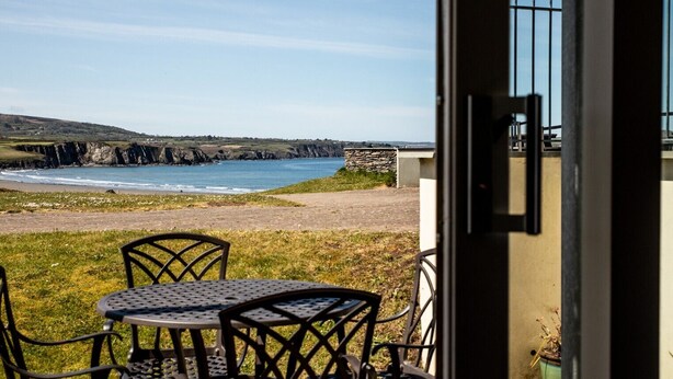 Une vue sur la côte depuis une pièce qui comprend une table et des chaises, un mur en pierre et un ciel dégagé.