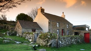 Une maison en pierre avec une façade blanche, une porte rouge et un mur de pierre à l’avant.