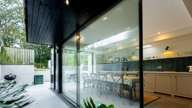 A modern kitchen with glass doors, a dining area with wooden chairs, and a view of the outdoors. - A stylish house for 6 in the heart of Newport, Pembrokeshire (Newport)