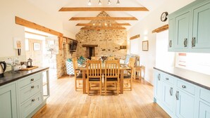 A rustic kitchen with a stone wall, wooden beams, and a dining area with a table and chairs. - A beautiful barn conversion nestled amongst the hills.. (Crymych)