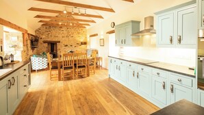 A kitchen with light blue cabinets, wooden beams, a stone wall, and a dining area with wooden chairs and a table. - A beautiful barn conversion nestled amongst the hills.. (Crymych)