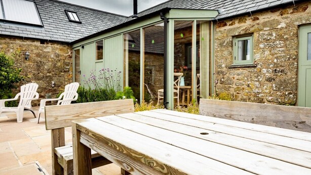 A rustic stone building with a wooden deck, outdoor seating, and a covered patio area. - A beautiful barn conversion nestled amongst the hills.. (Crymych)