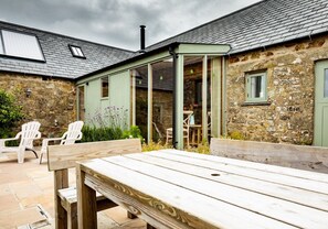 Een rustiek stenen gebouw met een houten terras, buiten zitplaatsen en een overdekte patio.