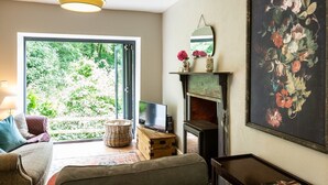Ein gemütliches Wohnzimmer mit Kamin, Fernseher und einem großen Fenster mit Blick auf Grünflächen.