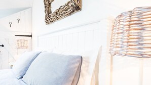 A bedroom with a white headboard, striped bedding, and a woven wall art piece. - A gorgeous property right on the beach - perfect for families (Newport)