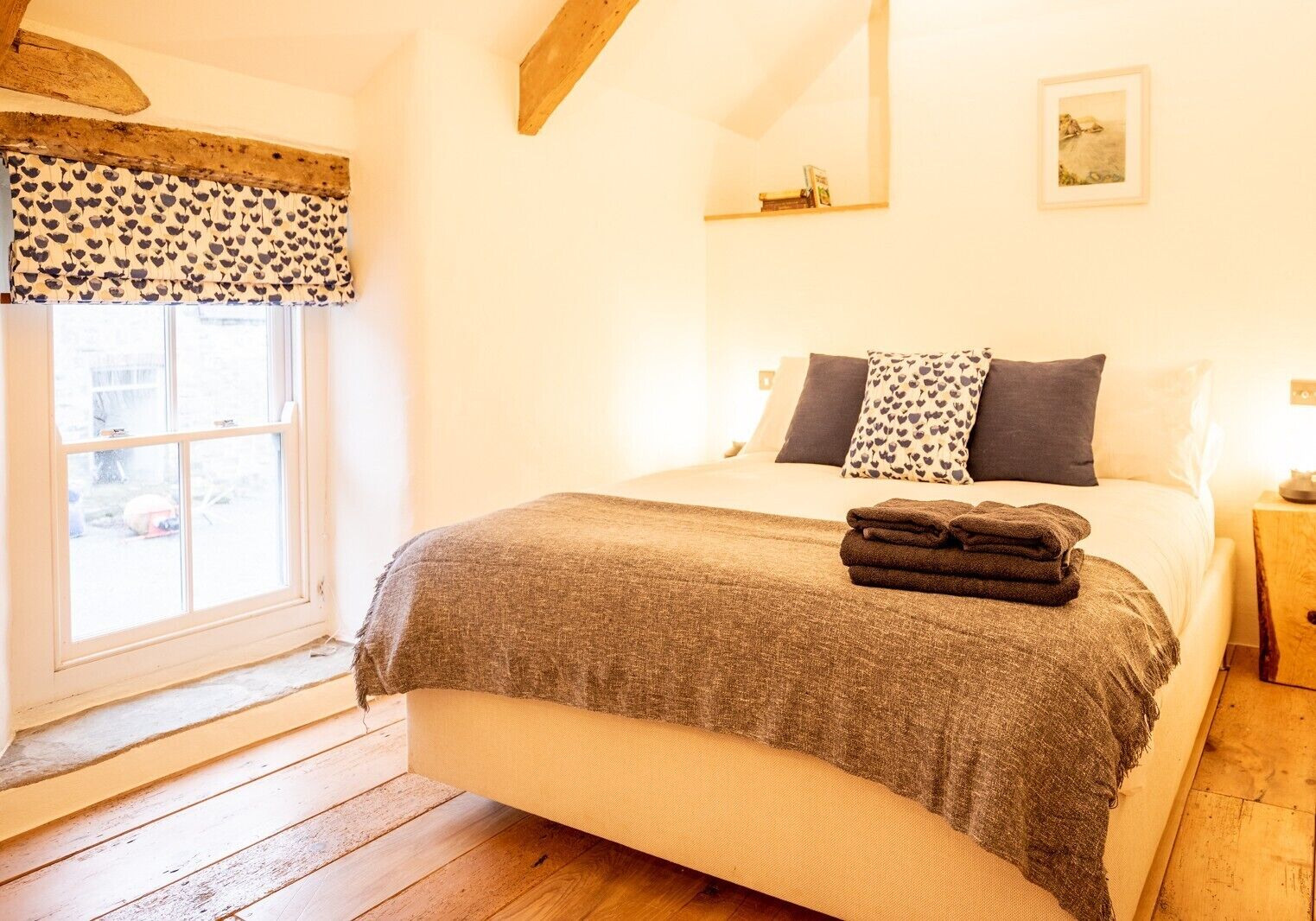 A bedroom with a bed, pillows, a window, and a wooden floor.