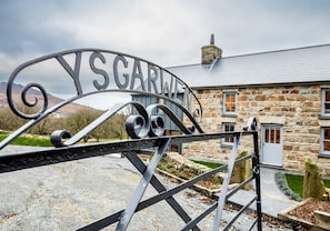 A metal gate with the inscription "YSGARTH" in front of a stone building with a grey roof.
