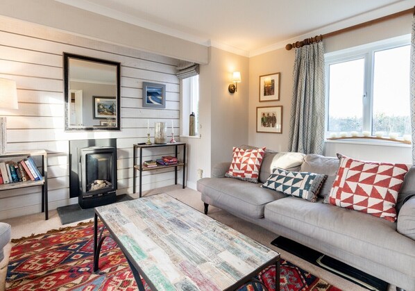 A cozy living room with a fireplace, a sofa with patterned cushions, a coffee table, and a bookshelf.