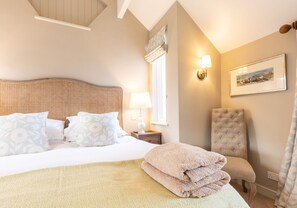 A neatly made bed with floral pillows, a bedside lamp, a chair, and a folded towel on the floor.