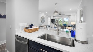 A modern kitchen with a stainless steel sink, a built-in dishwasher, and a dining area with a table and chairs. - Fripper Upper: 1st Floor, Just for TWO, MARSH Views, FREE Coffee/Tea/Creamer, Club Cards Available! (Fripp Island)