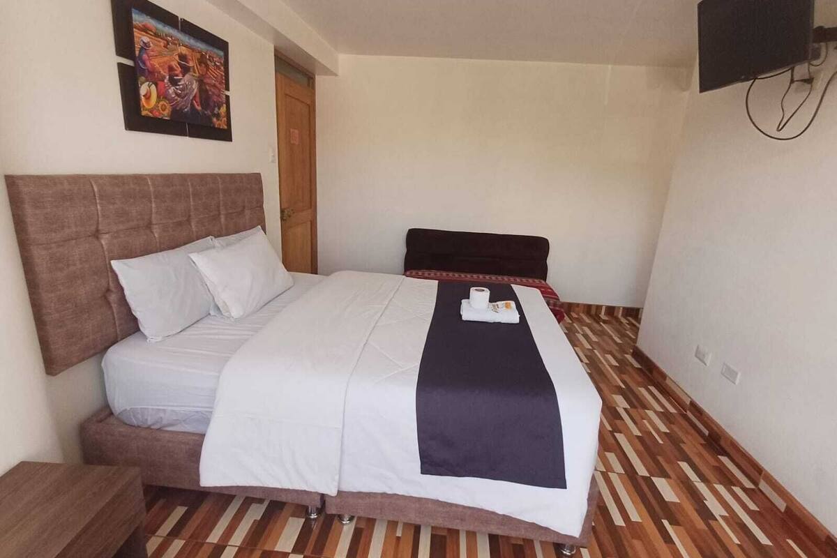 A hotel room with a large bed, a wooden floor, a painting on the wall, and a TV mounted on the wall.