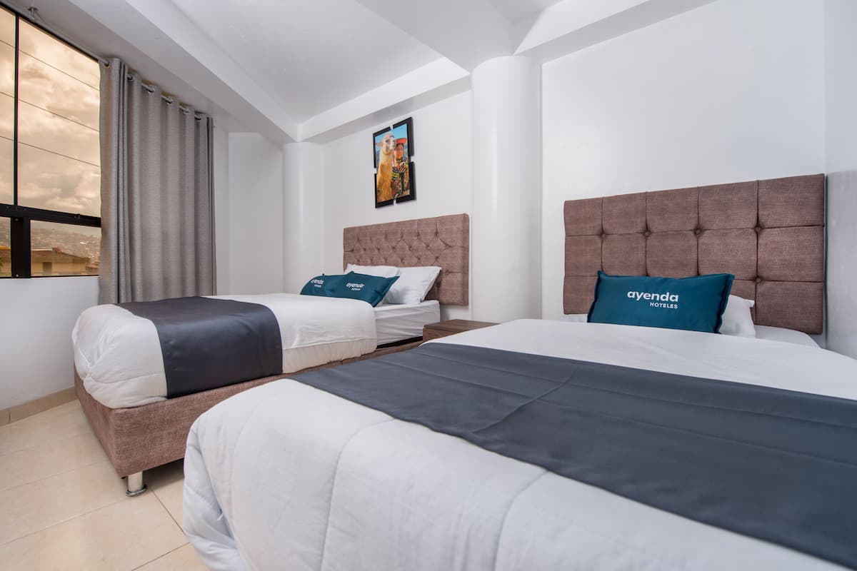 A hotel room with two beds, a large window with curtains, a tufted headboard, and a framed picture on the wall.