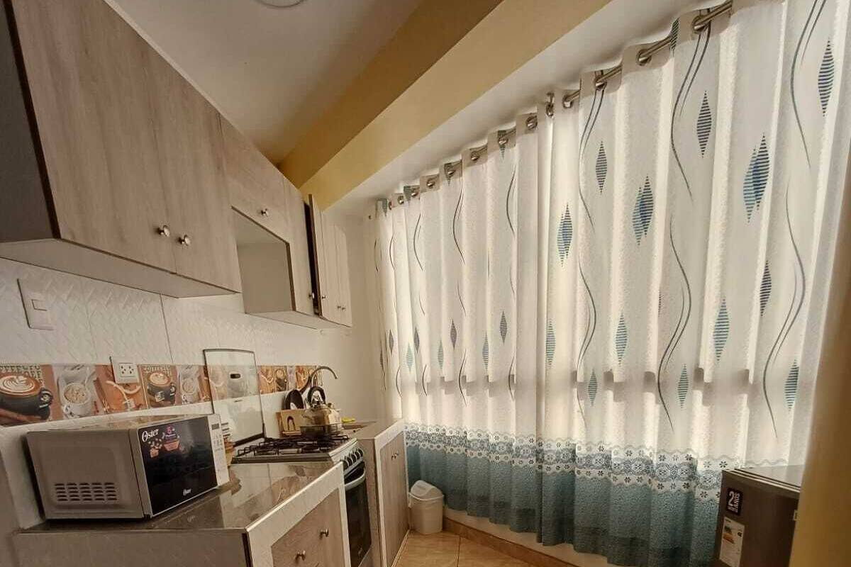 A kitchen with a built-in microwave, stove, and sink. There is a trash bin and a refrigerator in the corner.