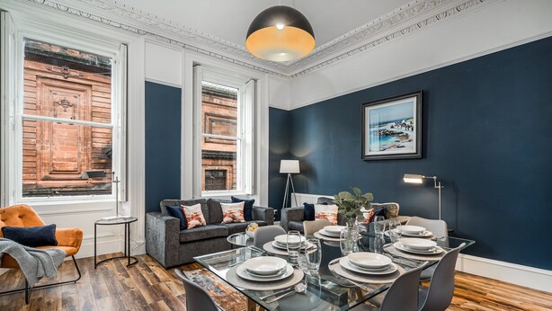 A dining area with a glass table set for six, surrounded by grey chairs.