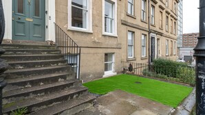 A townhouse with a green door, a small front yard with a lawn, and a set of stone steps leading to the entrance.