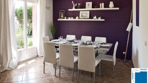 A dining area with a purple wall, white shelves, and a view of greenery outside.