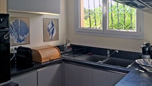 Une cuisine moderne avec un plan de travail noir, un évier en acier inoxydable et un four encastré. On y trouve deux machines à café fixées au mur et un bol décoratif posé sur le plan de travail.