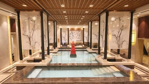 Un espace de bien-être doté d’une piscine centrale, de colonnes en bois et d’un élément décoratif rouge.