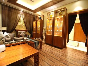A room with a wooden table, a sofa, a lamp, and a cabinet with glass doors. - Yi Jin Hotel (Harbin)
