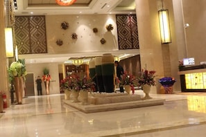 A hotel lobby with a reception desk, decorative plants, and a modern chandelier. - Yi Jin Hotel (Harbin)