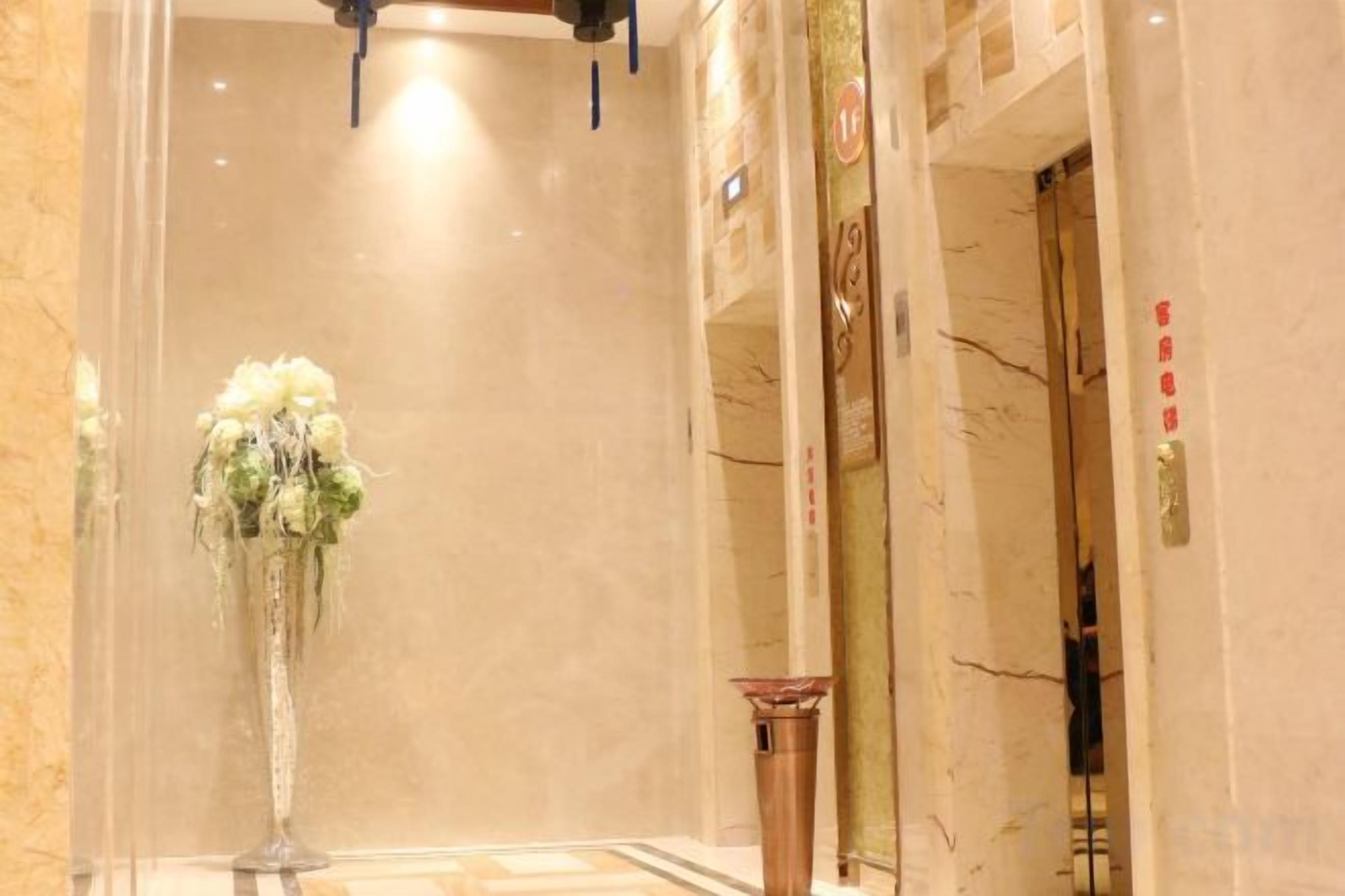 A marble-floored hallway with a tall vase of flowers, a door with a golden handle, and a wall with a decorative pattern.