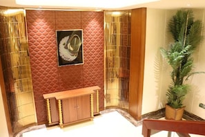 A lobby with a patterned wall, a wooden bench, and a potted plant. - Yi Jin Hotel (Harbin)
