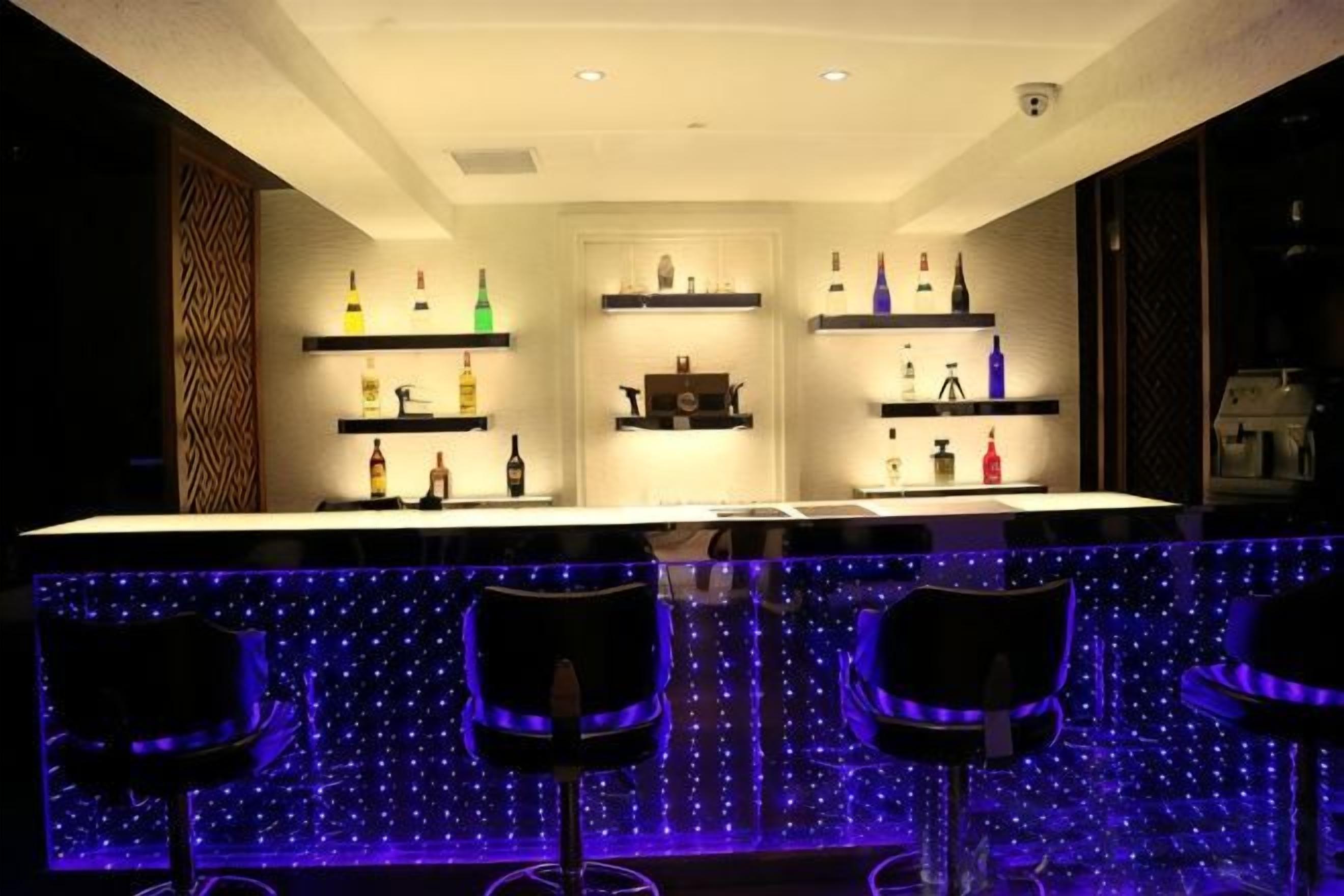 A bar area with a counter, shelves with bottles, and bar stools.