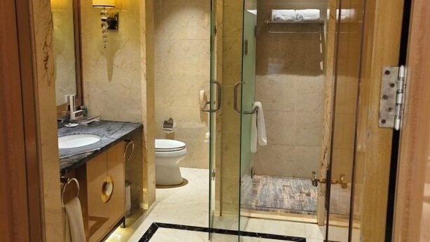A bathroom with a glass-enclosed shower, a marble sink, and a toilet. - Yi Jin Hotel (Harbin)