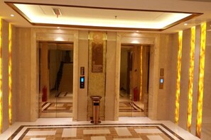 A hotel lobby with a marble floor, a central column, and a staircase leading to an upper floor. - Yi Jin Hotel (Harbin)