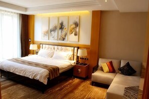 A hotel room with a large bed, a sofa, and a nightstand with lamps. - Yi Jin Hotel (Harbin)