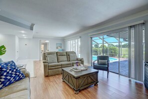 Relax in this inviting living room with a large sectional sofa, wooden coffee table, and sliding glass door leading to an outdoor area.