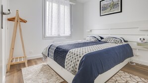 A bedroom with a bed, a wooden easel, a window with curtains, a painting on the wall, and a bedside table with a lamp. - L'Amarillo - Apt 1 chambre vielle ville (Nancy)