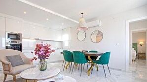 Un salon moderne avec une table basse en marbre, un fauteuil beige et un coin repas avec des chaises vertes.