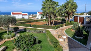 A landscaped garden with palm trees, a pathway, and a view of the sea. - Azzuro Villa by Estia (Hersonissos)