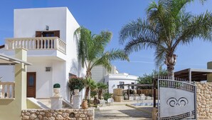 A modern building with a white facade, a stone wall, and a gated entrance. - Sunshine VIlla by Estia (Hersonissos)