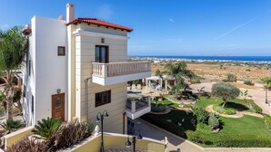 A two-story building with a balcony, a view of the sea, and a landscaped garden. - Sunshine VIlla by Estia (Hersonissos)