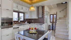 A modern kitchen with white cabinets, a glass dining table, and a stainless steel range hood. - Sunshine VIlla by Estia (Hersonissos)